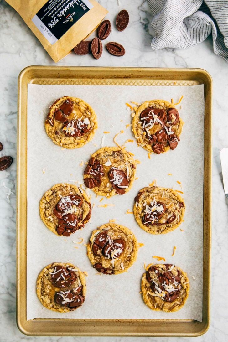 photo of coconut chocolate chip cookies on a gold tray on a marble tabletop with a bag of valrhona chocolate feves