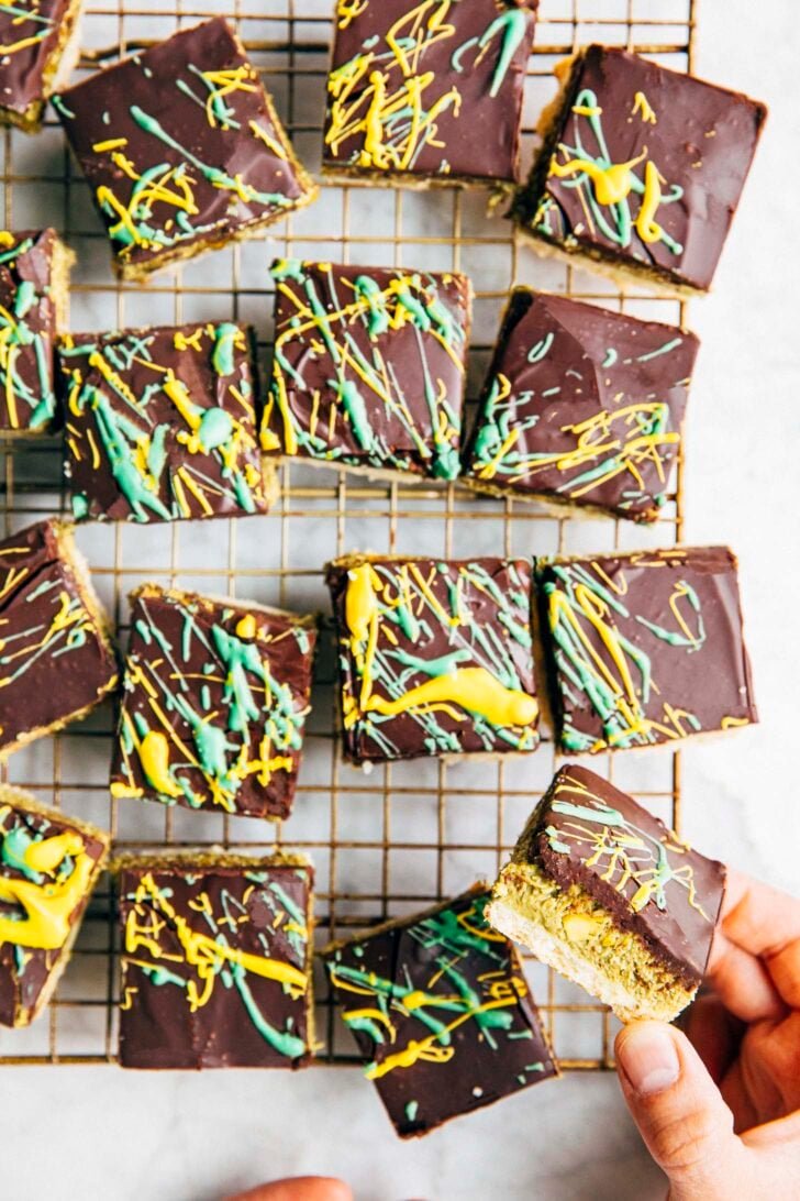 Photo of sliced Dubai chocolate millionaire bars on a wire rack with a hand reaching for a bar