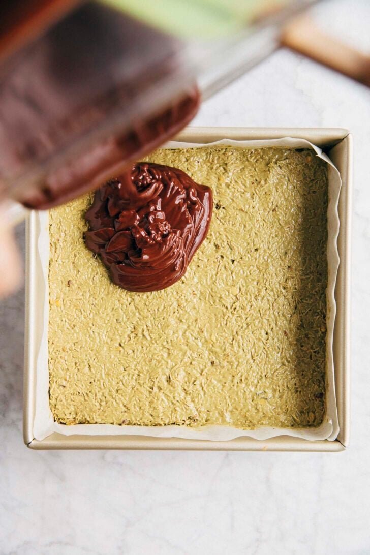 Photo of ganache being poured over the pistachio kataifi layer of the Dubai chocolate shortbread bars