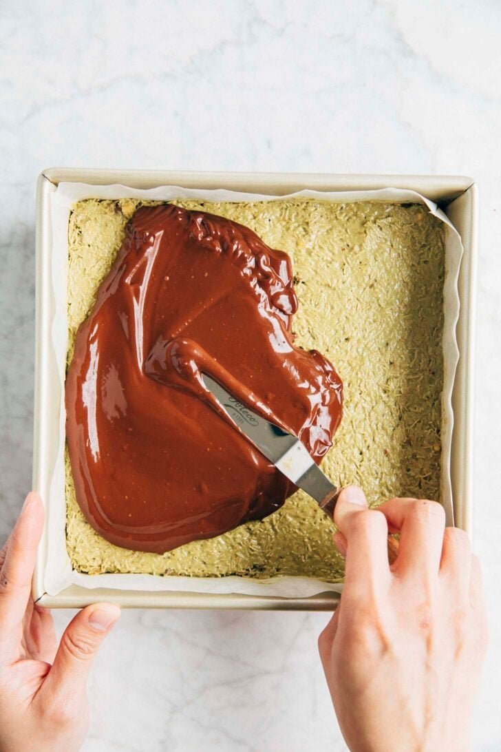 Photo of Michelle from Hummingbird High using an offset spatula to spread the chocolate ganache over the pistachio kataifi layer of the shortbread bars