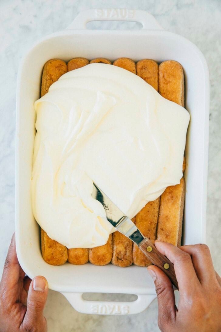 photo showing michelle of hummingbird high covering the first layer of soaked ladyfingers with zabaglione whipped cream