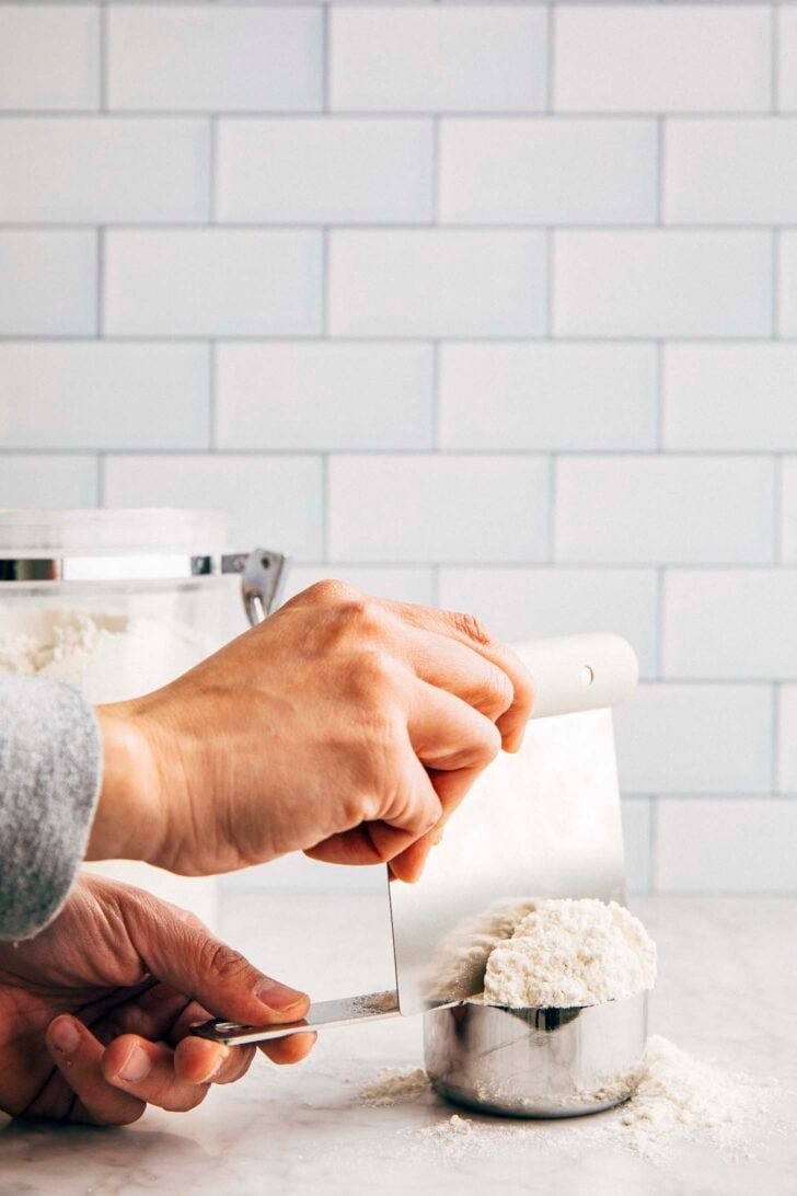 Photo of Michelle from Hummingbird High using a bench scraper to level the scooped flour in a measuring cup
