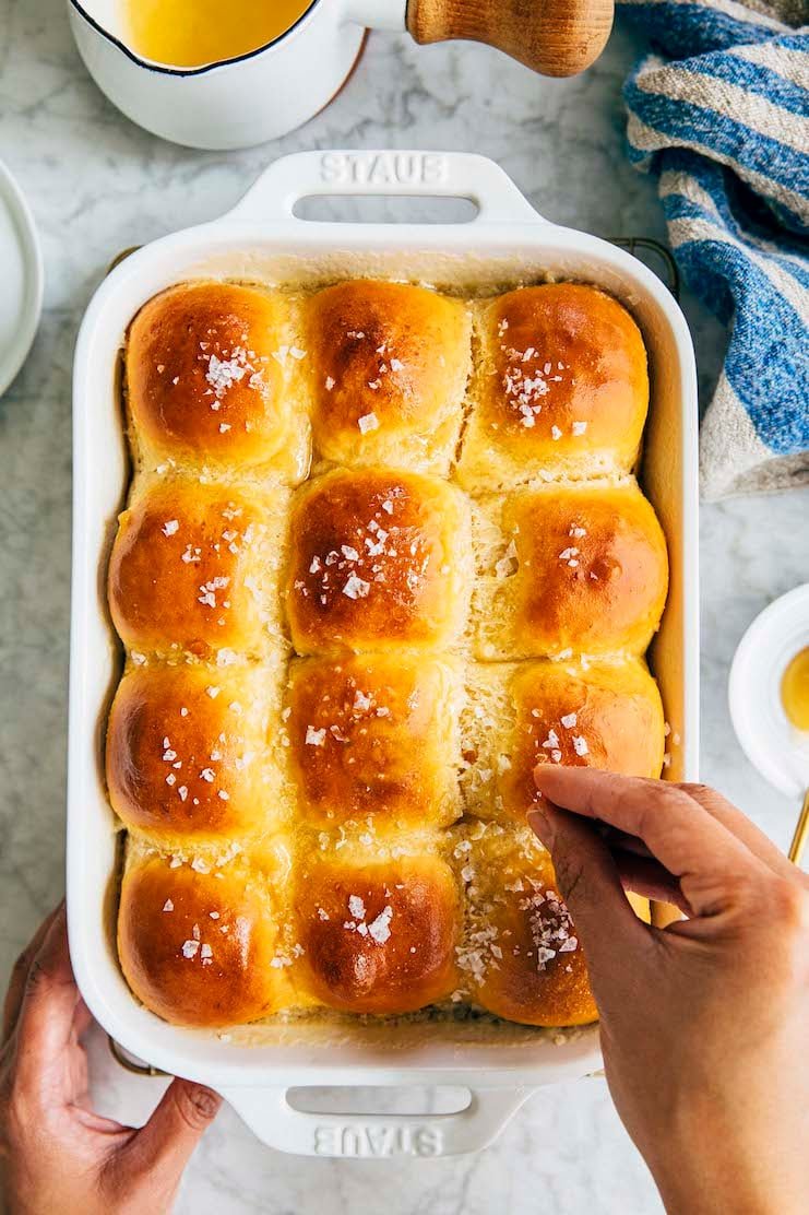 hand putting salt on salted honey parker house rolls
