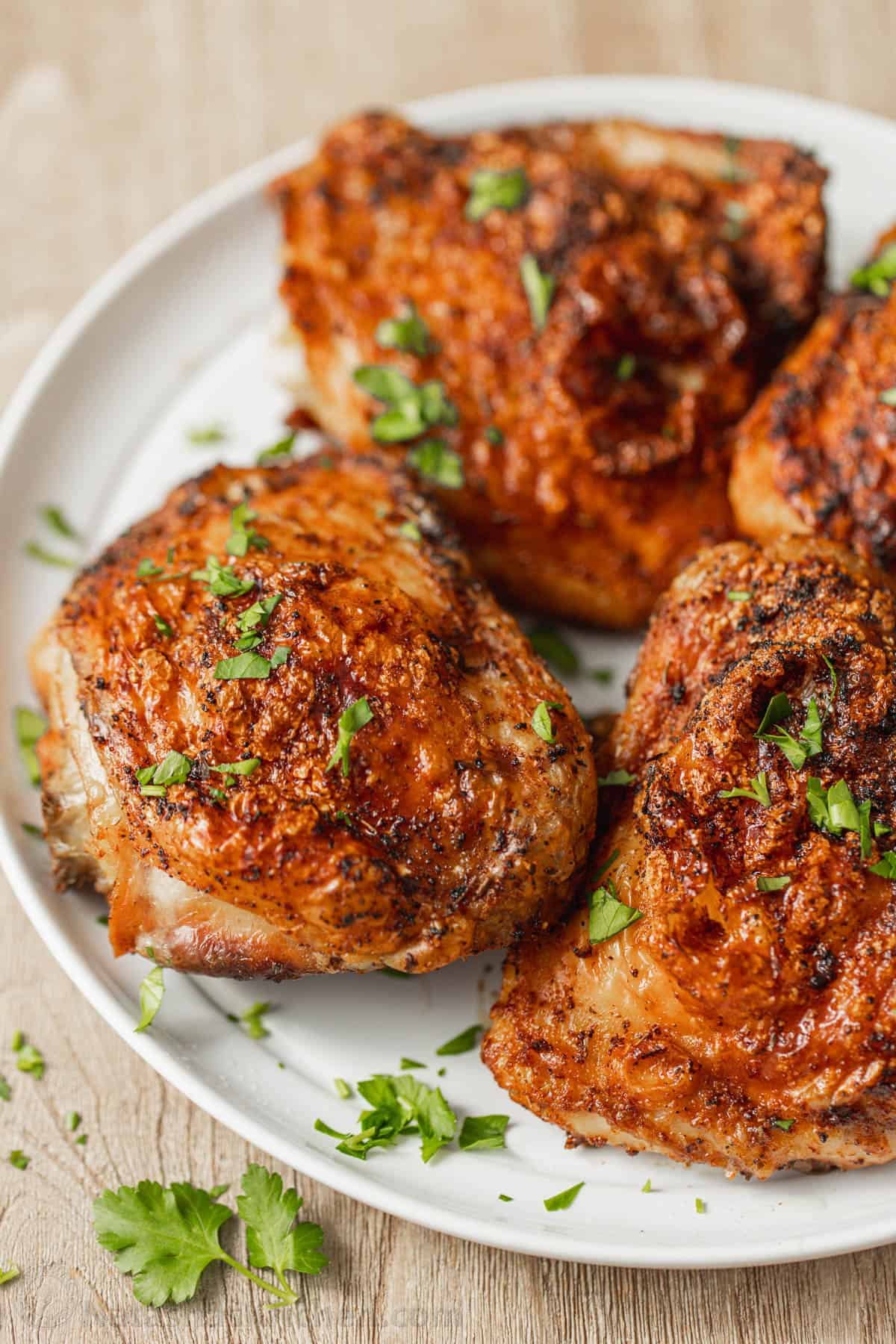 Air Fryer Chicken Thighs are crispy on the outside, so juicy and perfectly seasoned. An air fryer is the fastest way to cook chicken thighs! Four air fryer chicken things on a white plate garnished with freshly chopped parsley.