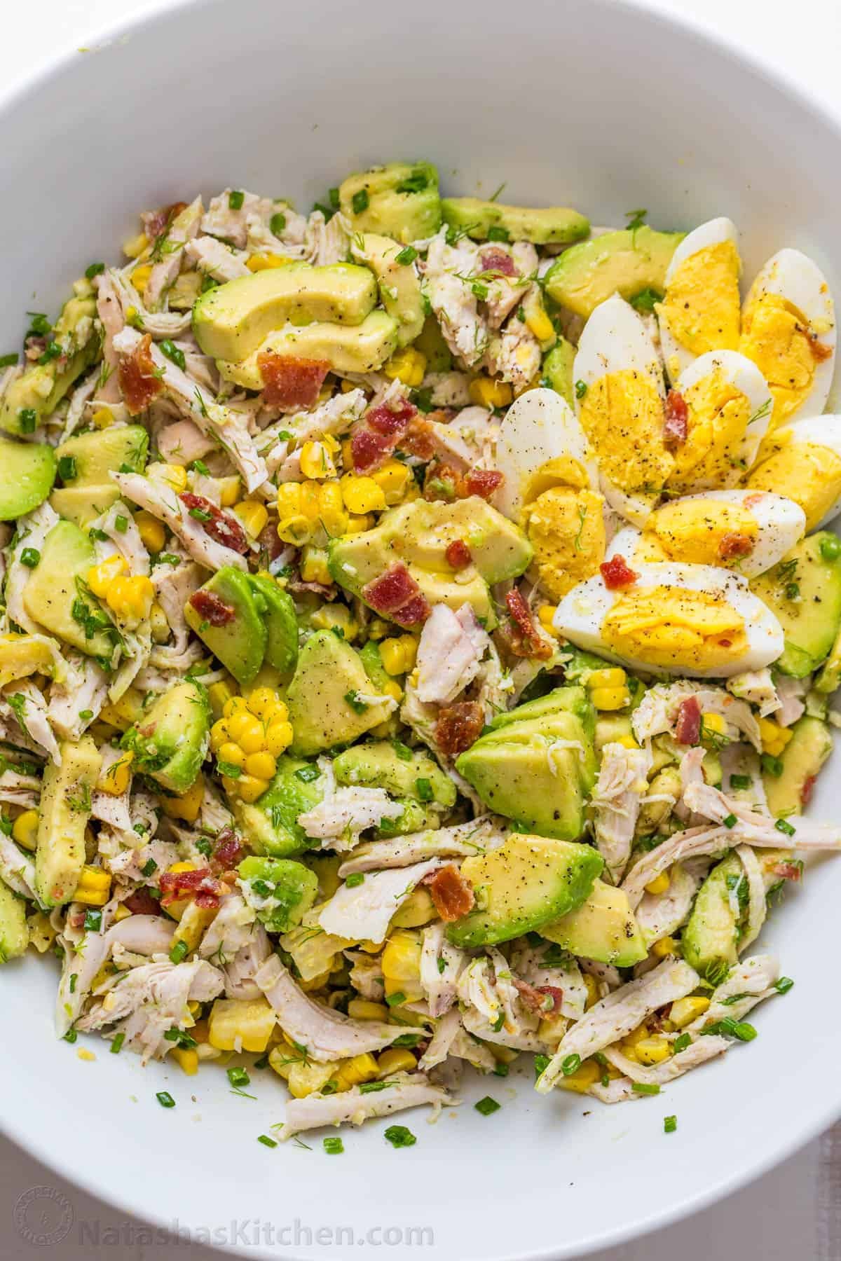 Avocado Chicken Salad in a white bowl with hardboiled eggs and bacon bits on top