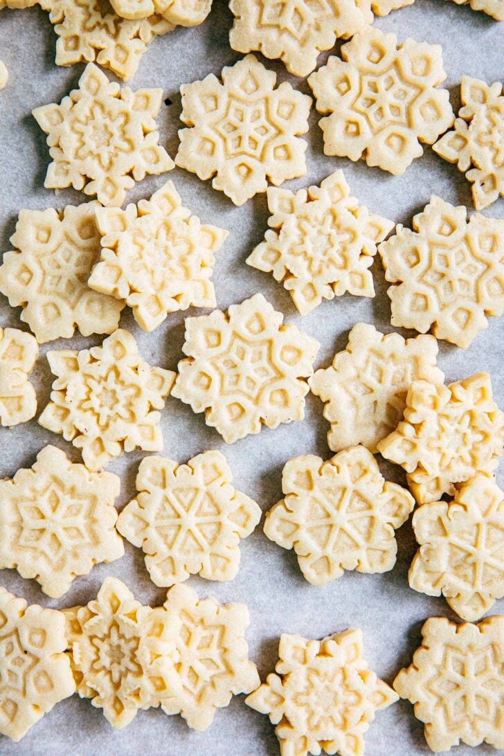 close up photo of cut out sugar cookies in the shape of snowflakes on parchment paper