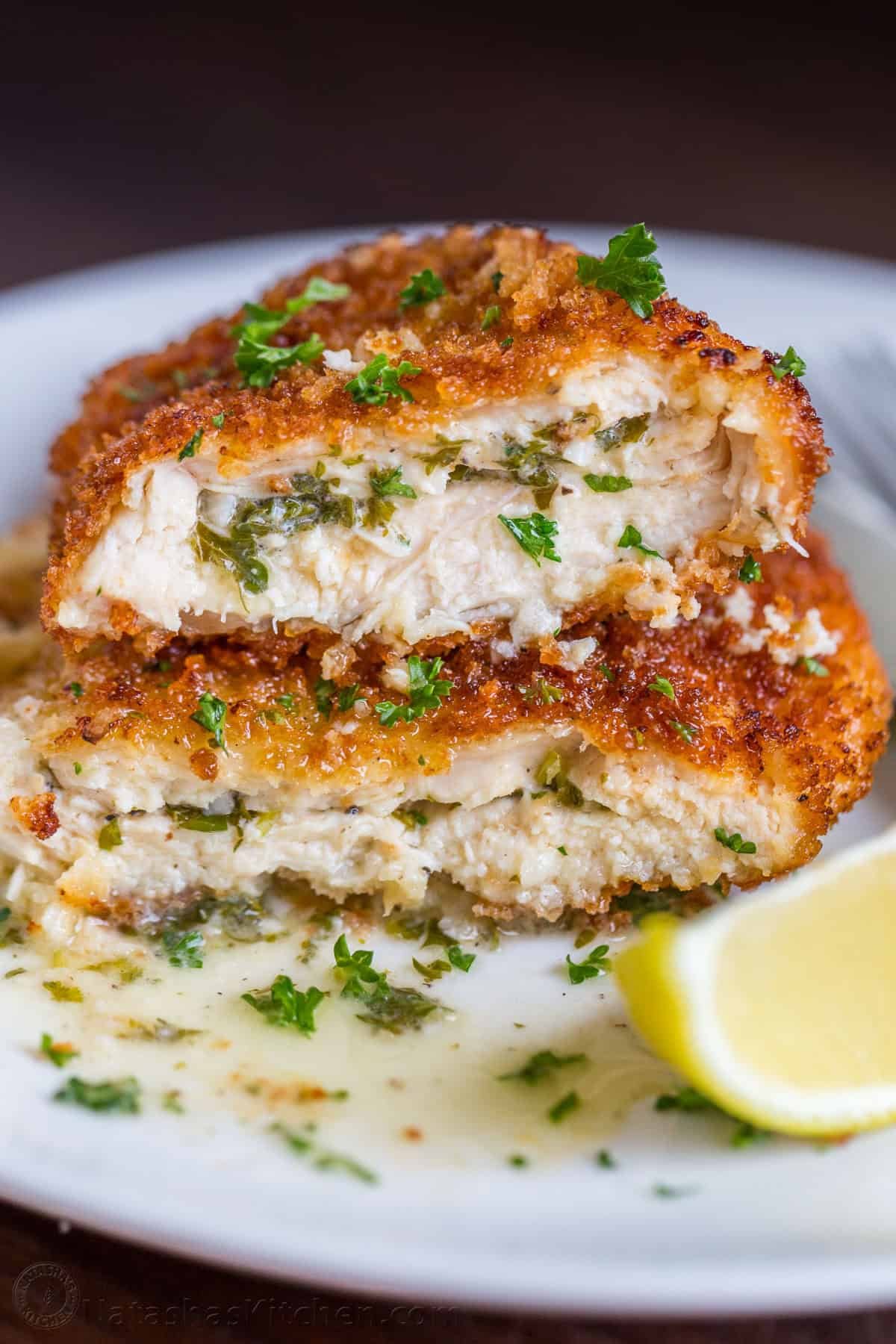 Chicken Kiev recipe cut in half on a white plate with lemon wedge and parsley garnish