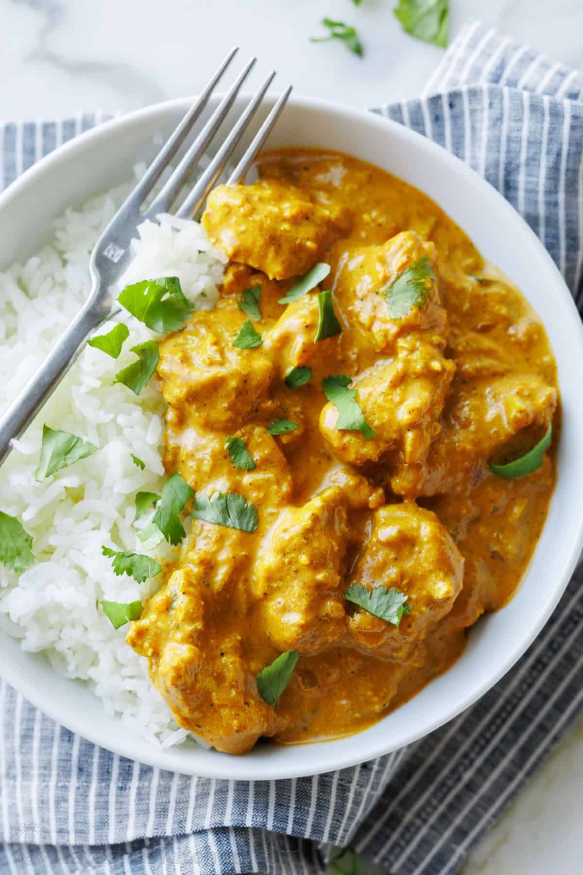 Chicken Korma is rich, creamy, and full of warm spices. This easy yet impressive dish brings the flavors of India to your kitchen. Serve over rice and enjoy! Chicken Korma and white rice in a dish with a fork, garnished with chopped cilantro