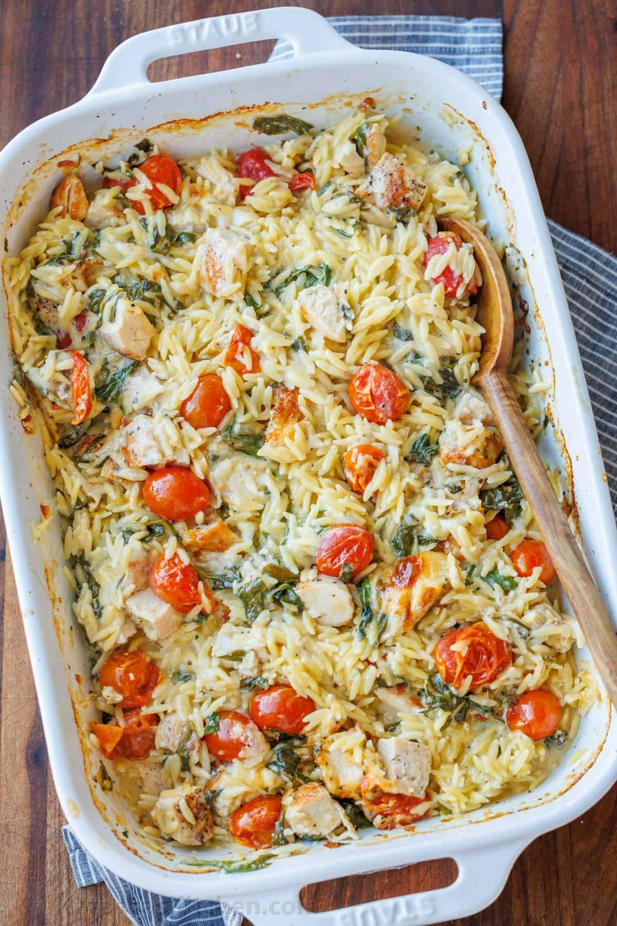 This Chicken Orzo Bake is an easy casserole that's creamy and cheesy. Mix it right in the dish, top it with cheese, and bake! Easy meal prep! Creamy chicken pasta casserole with cherry tomatoes in a white casserole dish