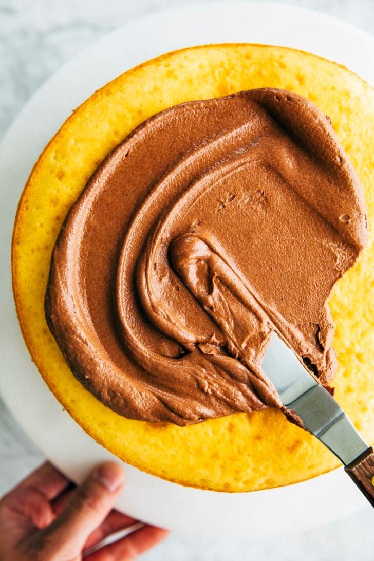 photo of chocolate fudge frosting being spread on a yellow cake