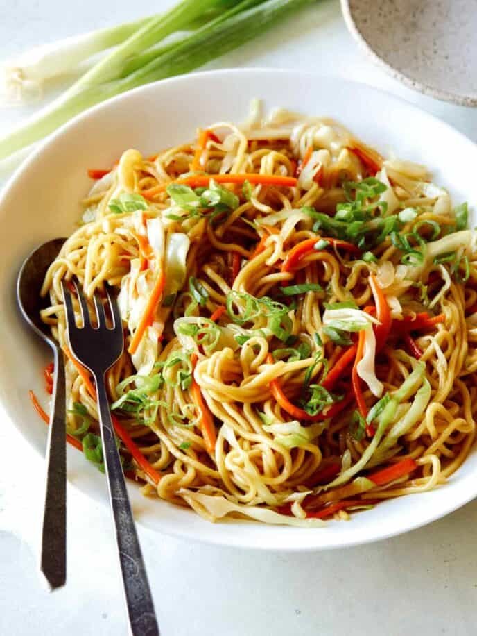Chow Mein Noodles in a big bowl with a fork and spoon in it to serve. 