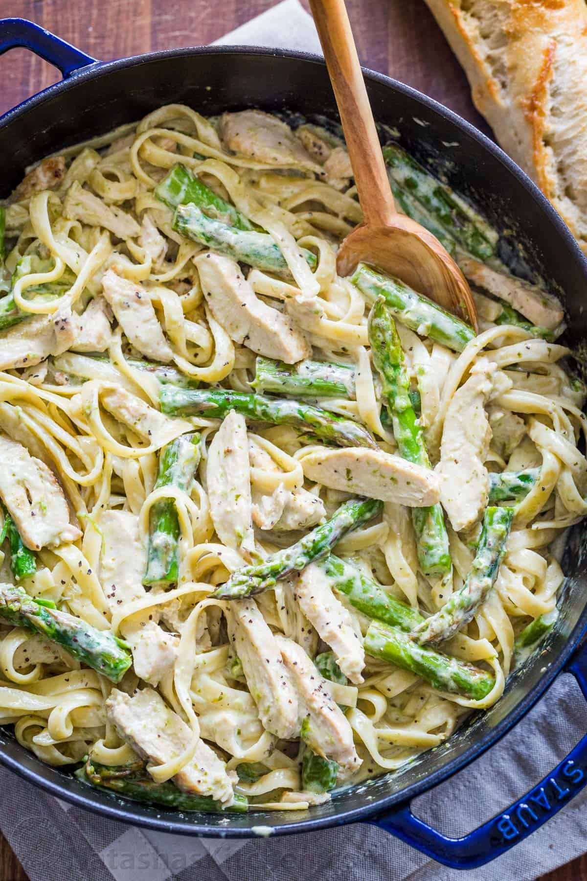 Chicken Pesto Pasta is an easy, 30-minute pasta dinner loaded with juicy chicken and asparagus. Try this crowd-pleasing pasta recipe! Chicken Pesto pasta in a blue skillet with asparagus and mixing spoon