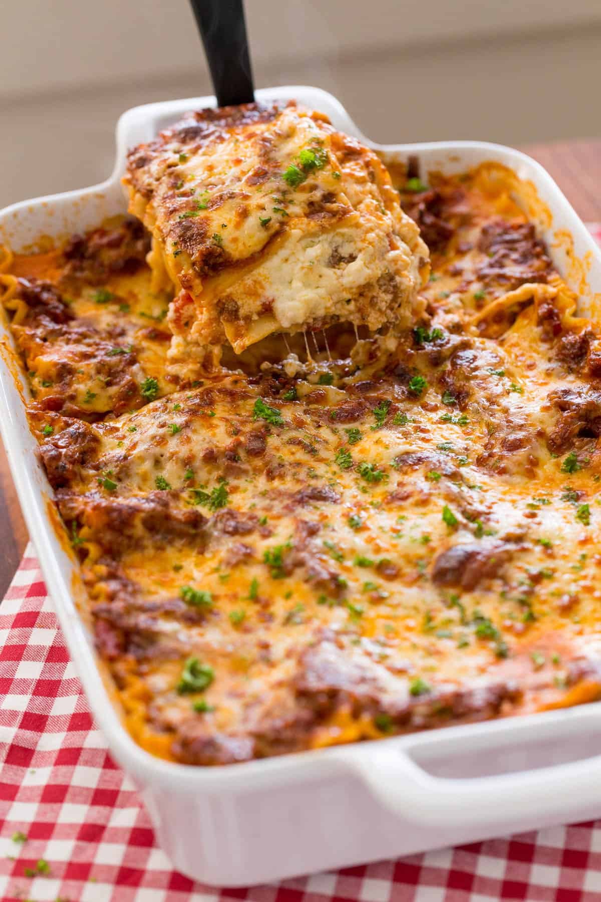 This easy Lasagna Recipe is meaty, cheesy, and flavorful. Perfect for a weeknight dinner or feeding a crowd, readers agree it's the best! Piece of lasagna being lifted from baking dish