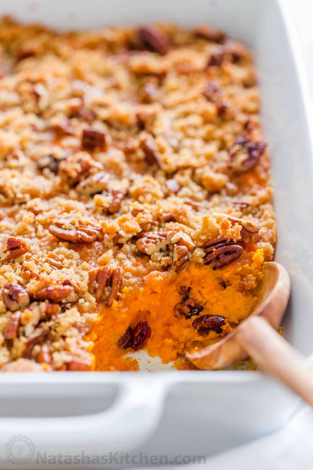 Sweet Potato Casserole with irresistible crunchy pecan topping. This sweet potato bake is smooth and puffs up while baking. A favorite Thanksgiving side! #sweetpotatocasserole #sweetpotatocasserolerecipe #sweetpotato #sweetpotatorecipes #natashaskitchen #thanksgiving #christmas Sweet potato casserole recipe with pecan streusel topping with serving spoon