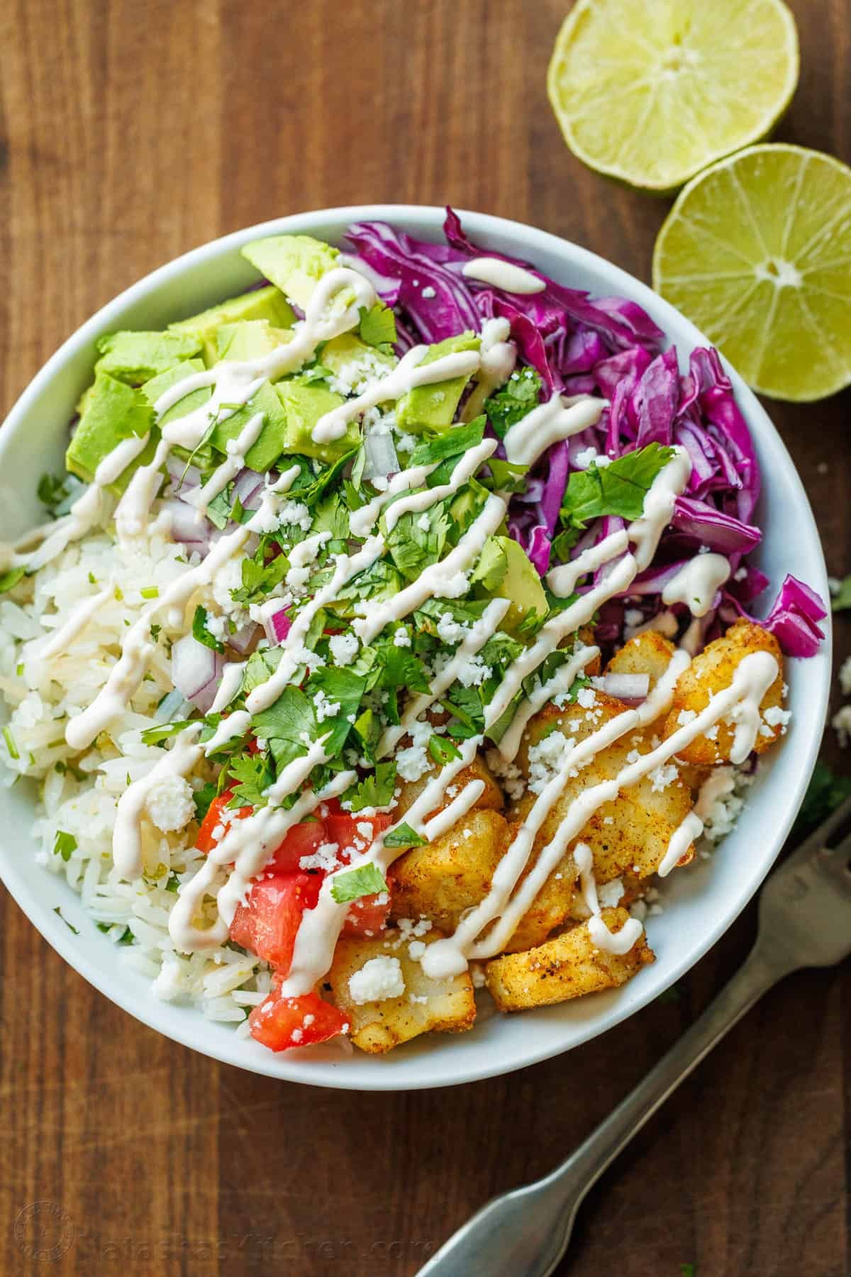 Our Fish Taco Bowl recipe is an easy taco night recipe. Mix flaky fish, Cilantro Lime Rice, toppings, and crema Sauce to serve in 30 minutes. Best Fish taco bowl recipe for Taco Tuesday with Lime and a fork