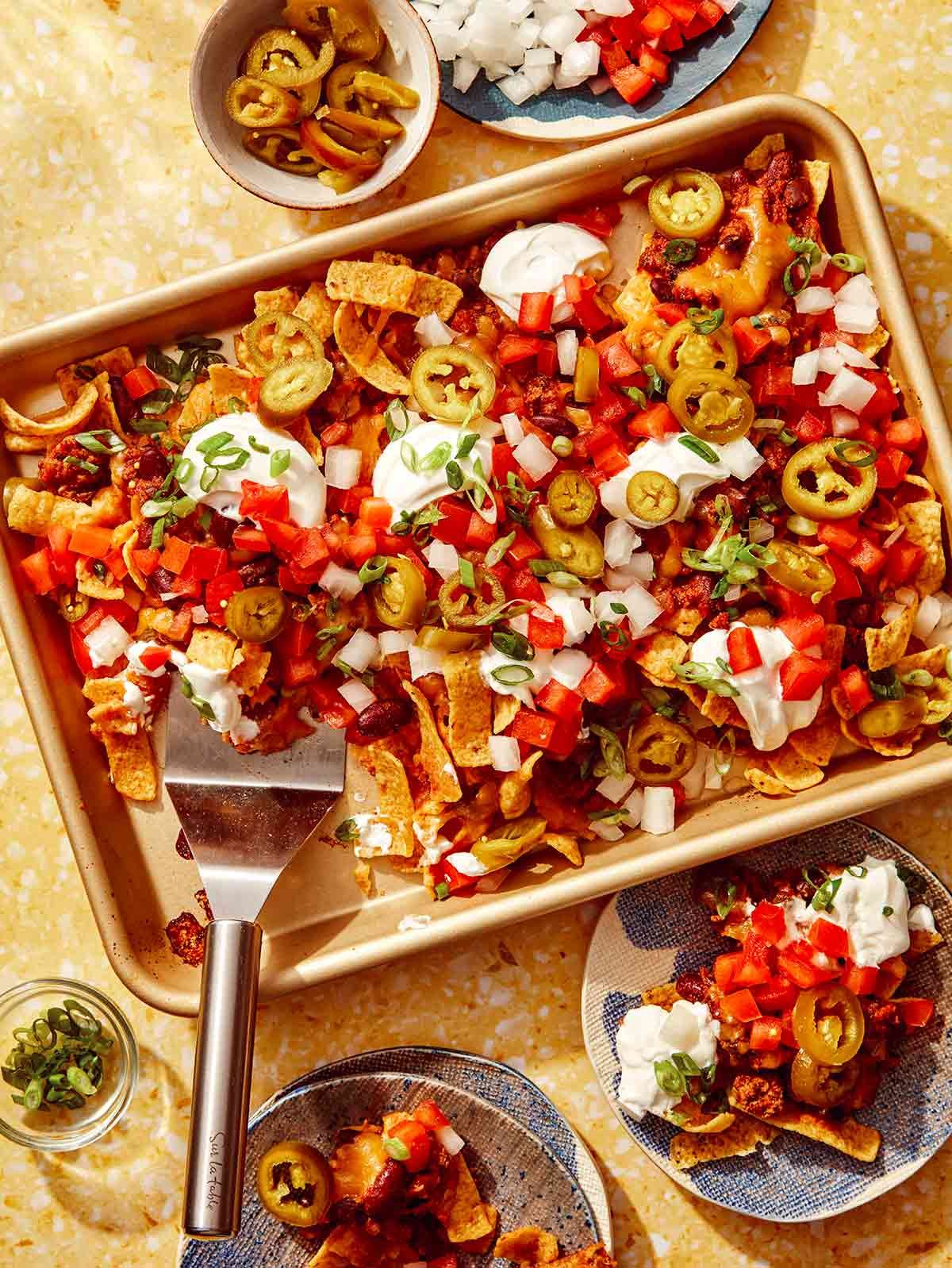 Frito pie recipe on a baking sheet with ingredients around it.
