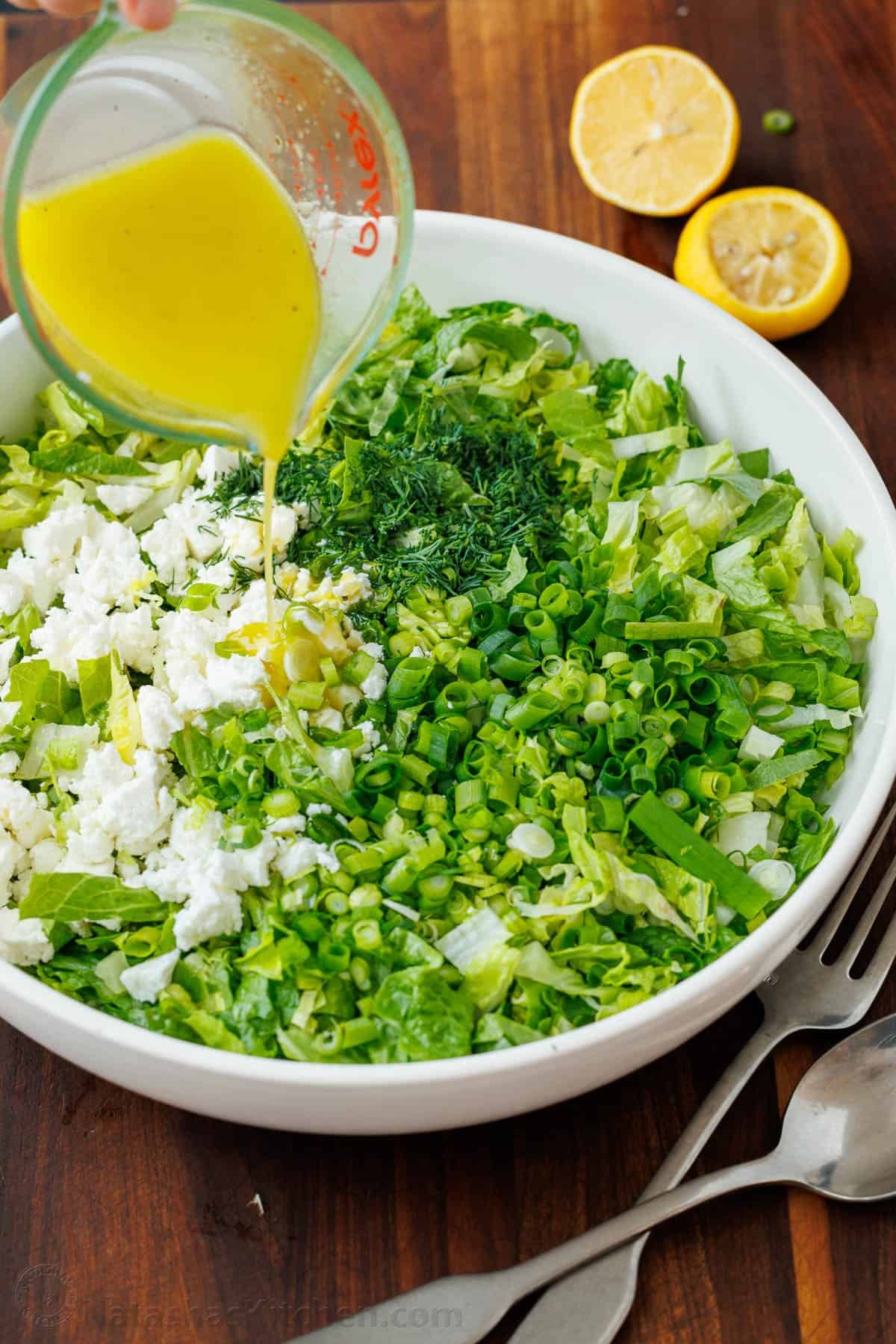 This traditional Maroulosalata recipe is an easy Greek Lettuce Salad with crisp romaine, feta, fresh herbs, and the best lemon dressing! Drizzling lemon dressing over Greek Maroulosalata salad in a white bowl