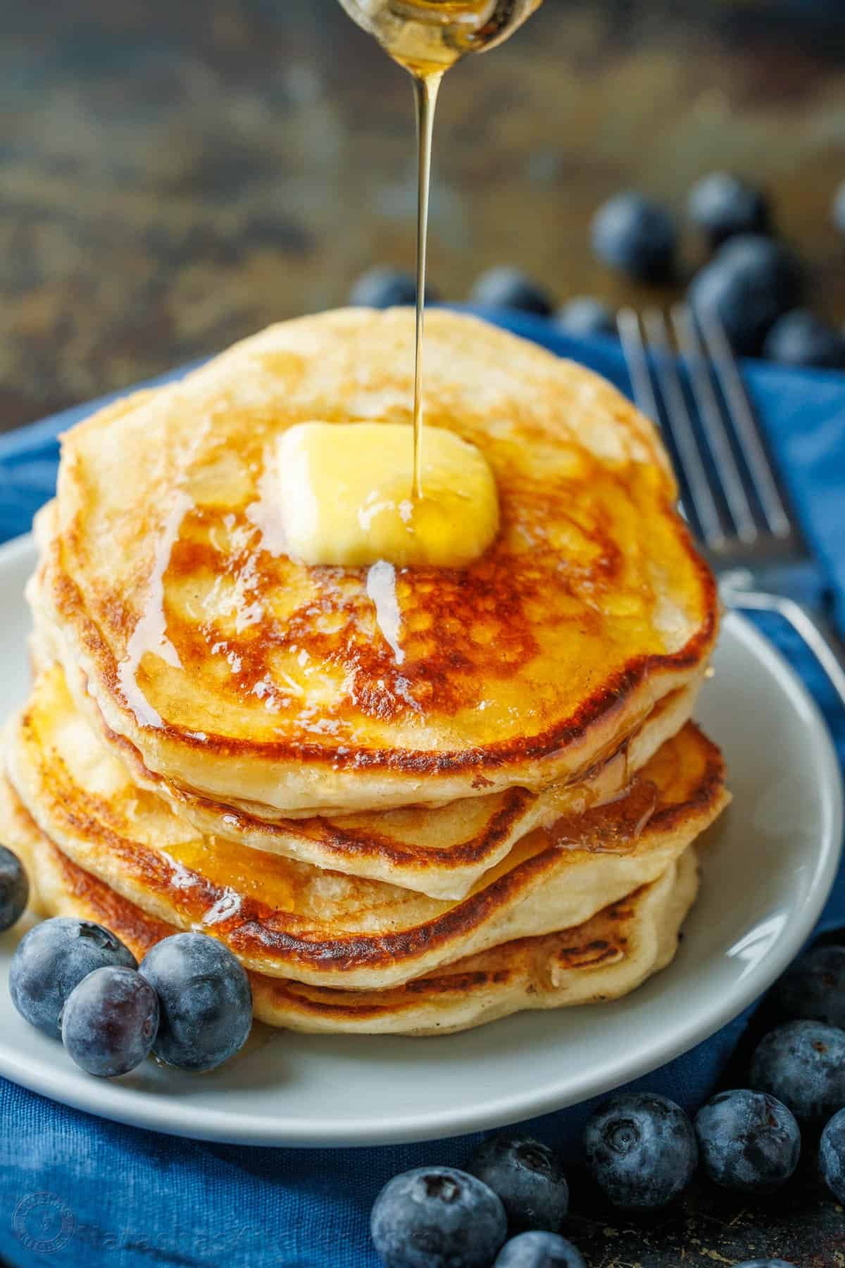 Overnight Sourdough Pancakes are easy! Mix everything before bed, leave at room temp overnight, and wake up to bubbly, ready-to-cook pancake batter. Sourdough Pancakes stacked on a plate with a pad of butter and maple syrup being poured over top.