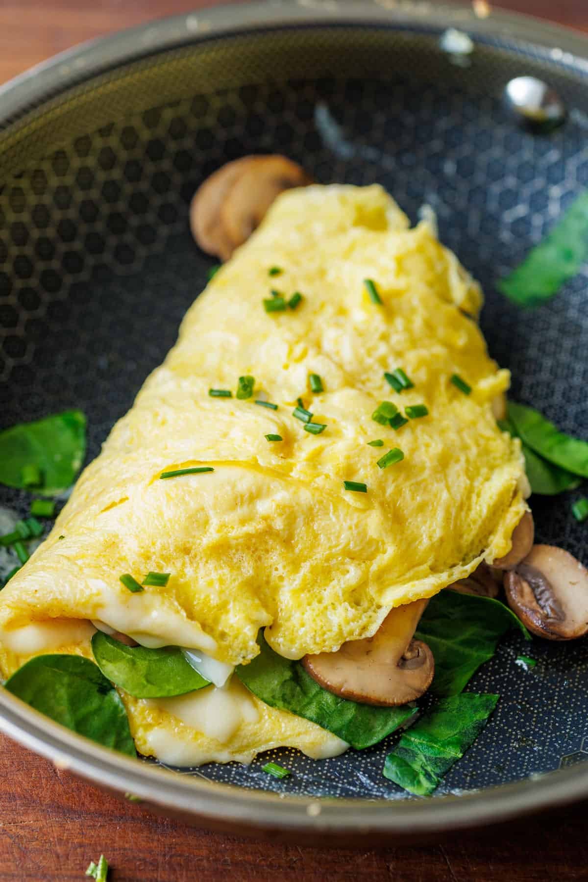 Omelette on a skillet stuffed with spinach and mushrooms