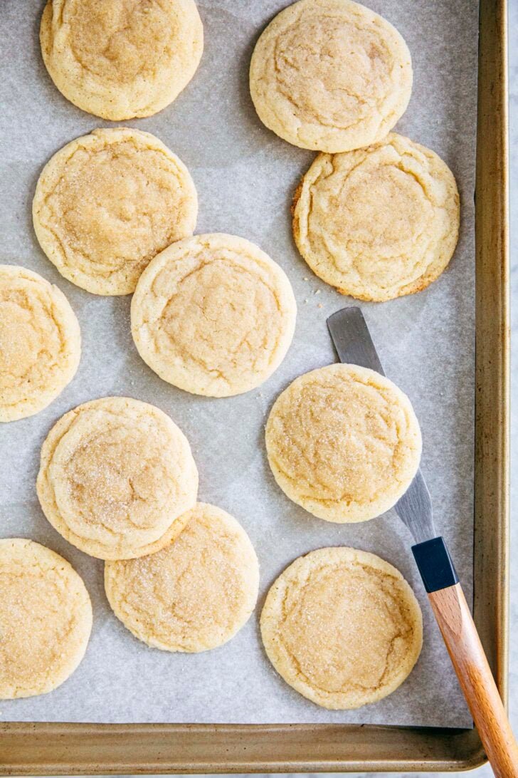 photo of drop sugar cookies on a gold sheet pan with an offset spatula
