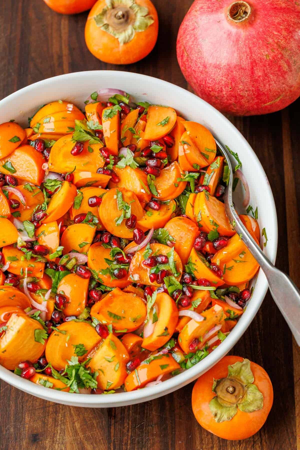 This easy persimmon pomegranate salad with lime cilantro dressing is one of the most exciting salads I've tried. It's vibrant and memorable! Persimmon Pomegranate Salad in a white bowl with fruit surrounding