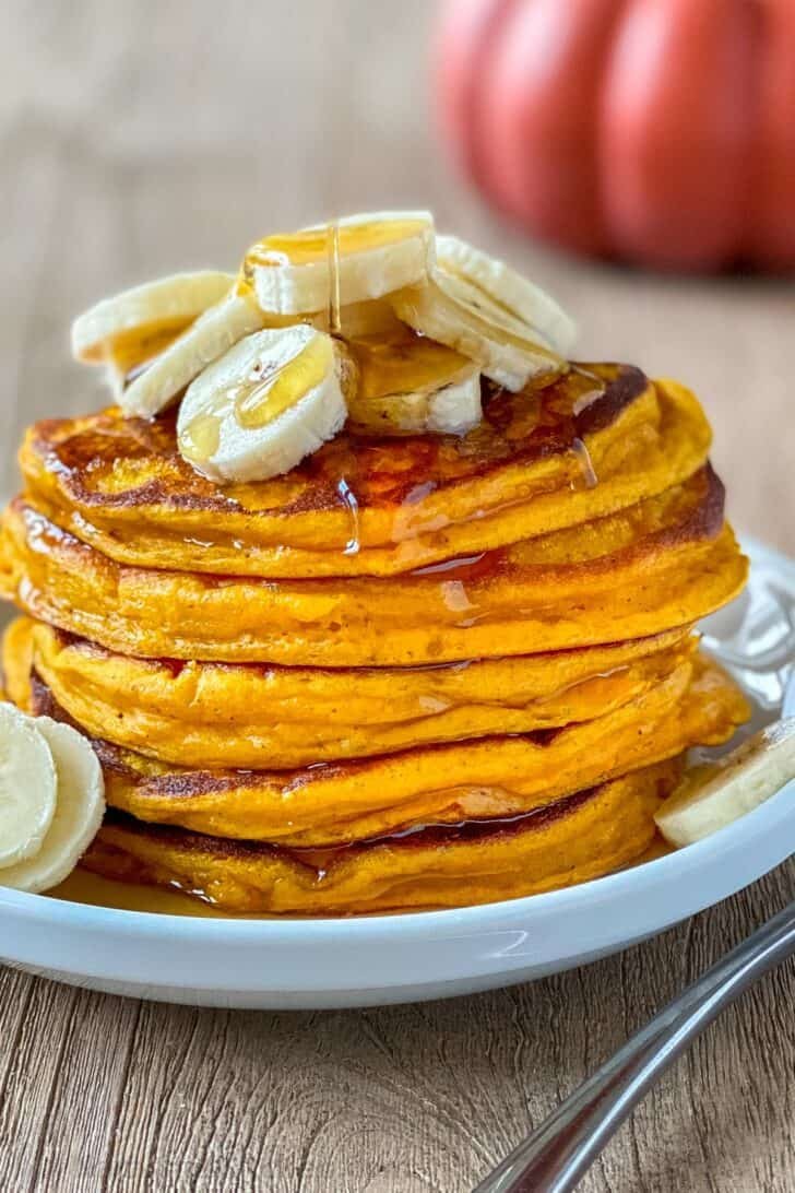 These pumpkin pancakes are so fluffy and the perfect Autumn breakfast. These are easy breakfast pancakes and have wonderful pumpkin flavor. #pumpkinpancakes #pumpkinrecipes Pumpkin pancakes stacked on a plate