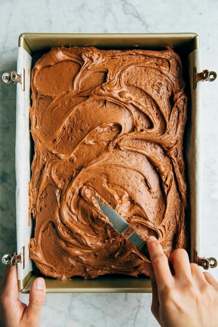 photo of michelle from hummingbird high spreading the chocolate cream cheese frosting on a sheet cake with an offset spatula
