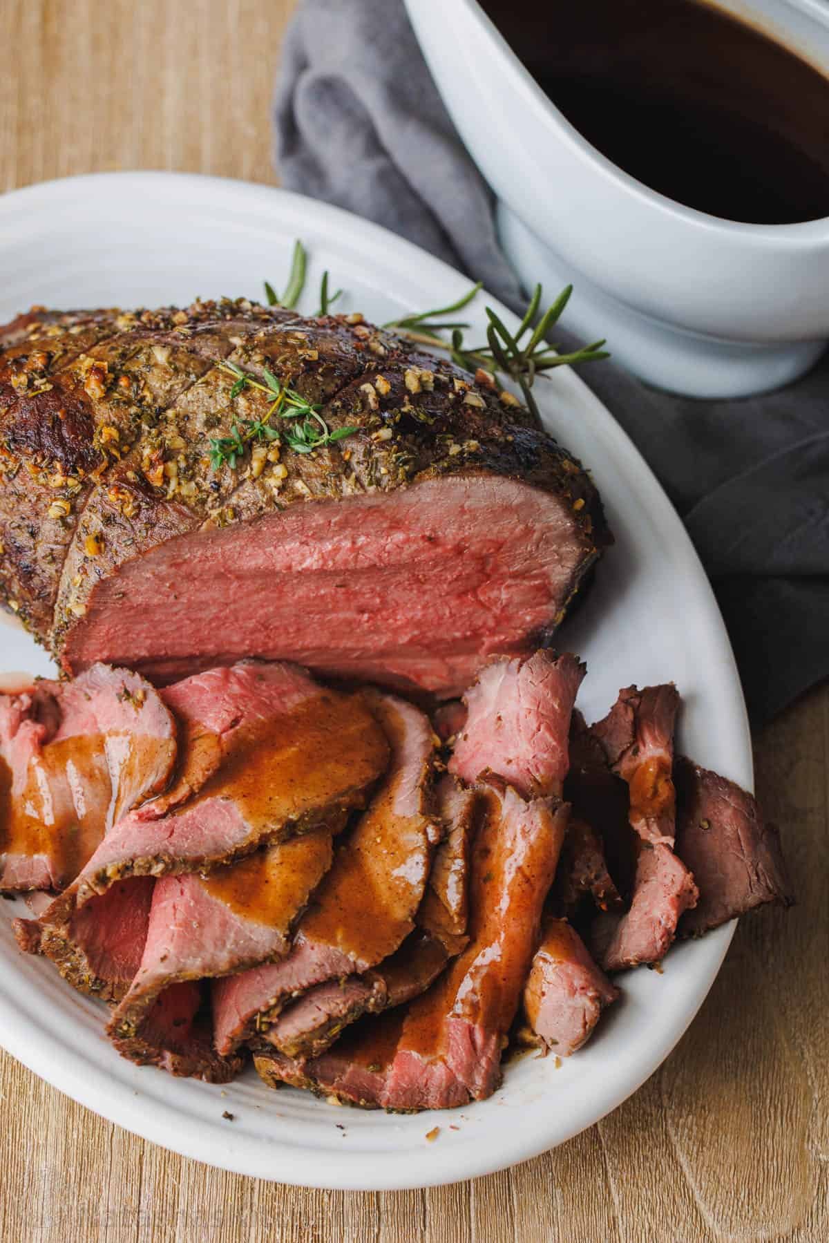 This simple, juicy Roast Beef with savory homemade pan gravy is just as impressive as any holiday roast. Every bite melts in your mouth. Roast beef sliced thinly on a platter, drizzled with beef gravy, next to a gravy boat.
