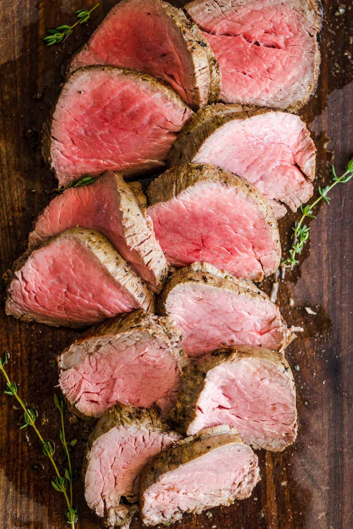 Roasted Beef Tenderloin is a showstopper! This tried and true easy method produces melt-in-your-mouth tender beef. How to trim, tie and cook beef tenderloin. #beeftenderloin #beeftenderloinrecipe #roastedbeeftenderloin #beef #steak #valentinesdaydinner #valentinesdayrecipes #natashaskitchen #dinner #tenderloin Roasted Beef Tenderloin Sliced into medallions on a cutting board