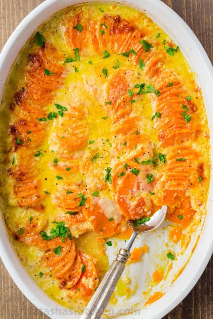 Scalloped sweet potatoes in a casserole dish with cheese and a spoon. 