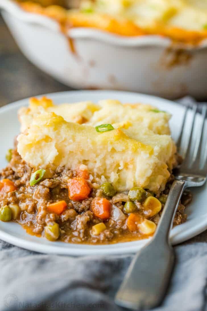 A homey and comforting Shepherd's Pie recipe with a meat and vegetable gravy sauce under a crown of creamy parmesan mashed potatoes. Slice of Shepherd's pie on a plate with fork