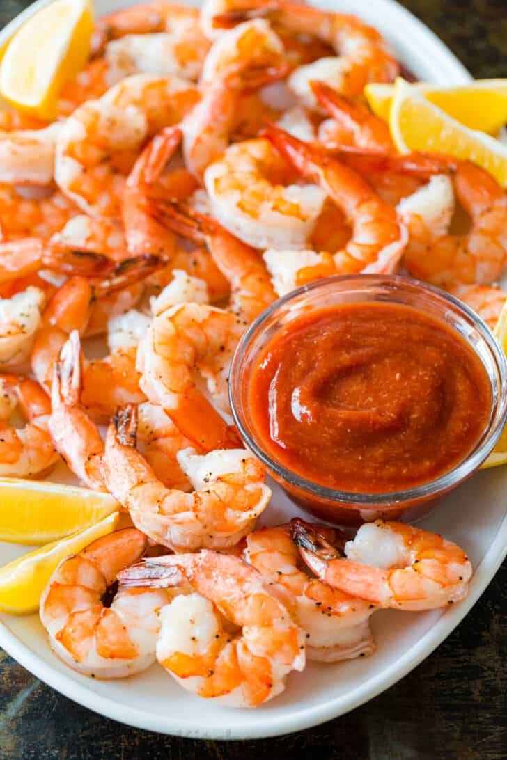 Homemade Shrimp Cocktail is impressive and easy with the best oven-baked shrimp and zesty shrimp cocktail sauce. Way better than a store-bought shrimp ring! #shrimpcocktail #shrimpcocktailrecipe #shrimpcocktailsauce #cocktailsauce #homemadecocktailsauce #condiments #dip #shrimp #appetizer #shrimpappetizer Shrimp cocktail recipe with zesty cocktail sauce served on a platter with lemon wedges