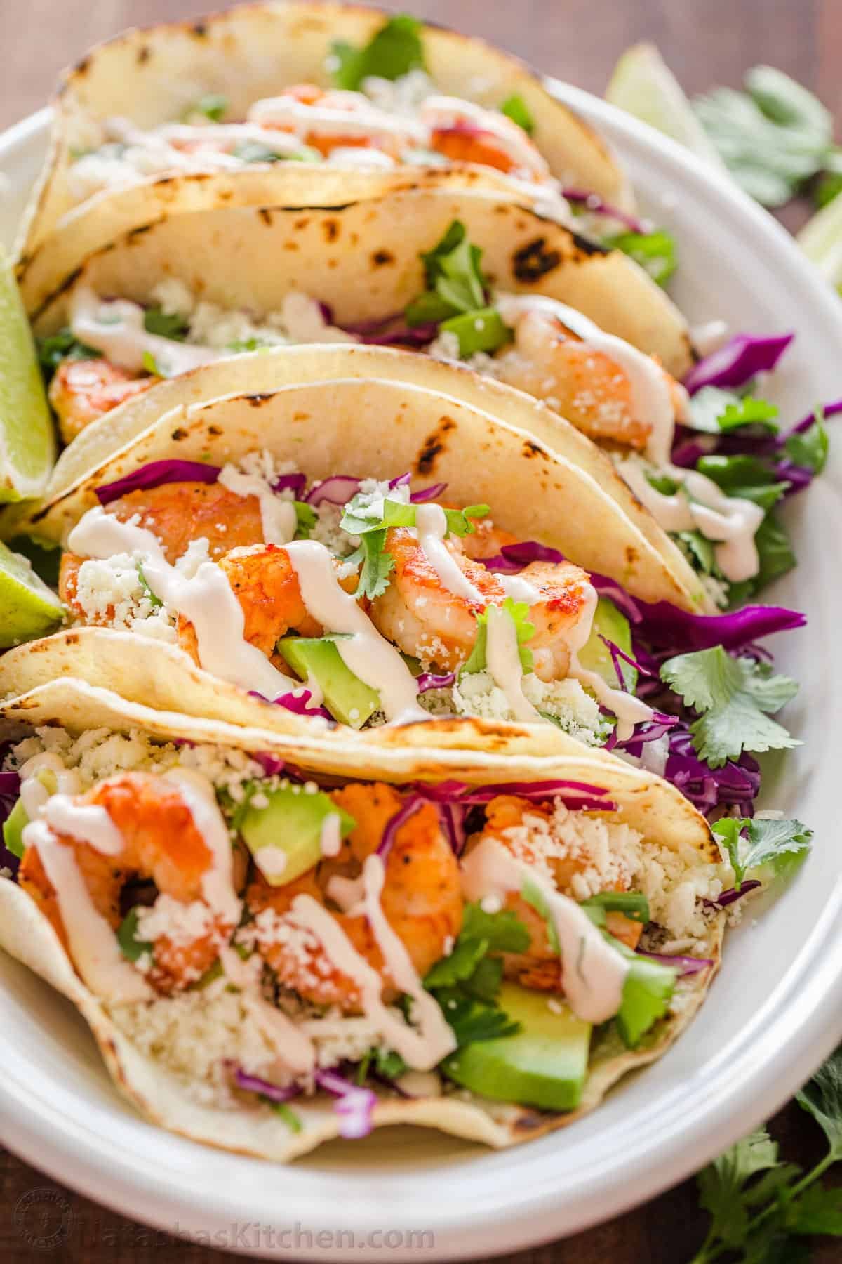 My easy Shrimp Tacos are loaded with shrimp, cabbage slaw, cotija cheese, and the BEST garlic-lime crema sauce. It's the only recipe you need! easy Shrimp tacos on a platter drizzled with garlic-lime crema shrimp taco sauce