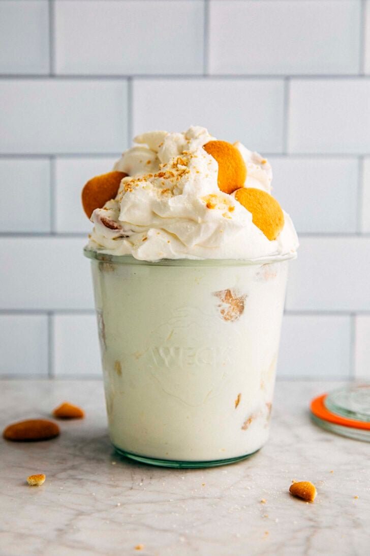 photo of a heaping small batch banana pudding in a pint jar with cookies scattered around the jar