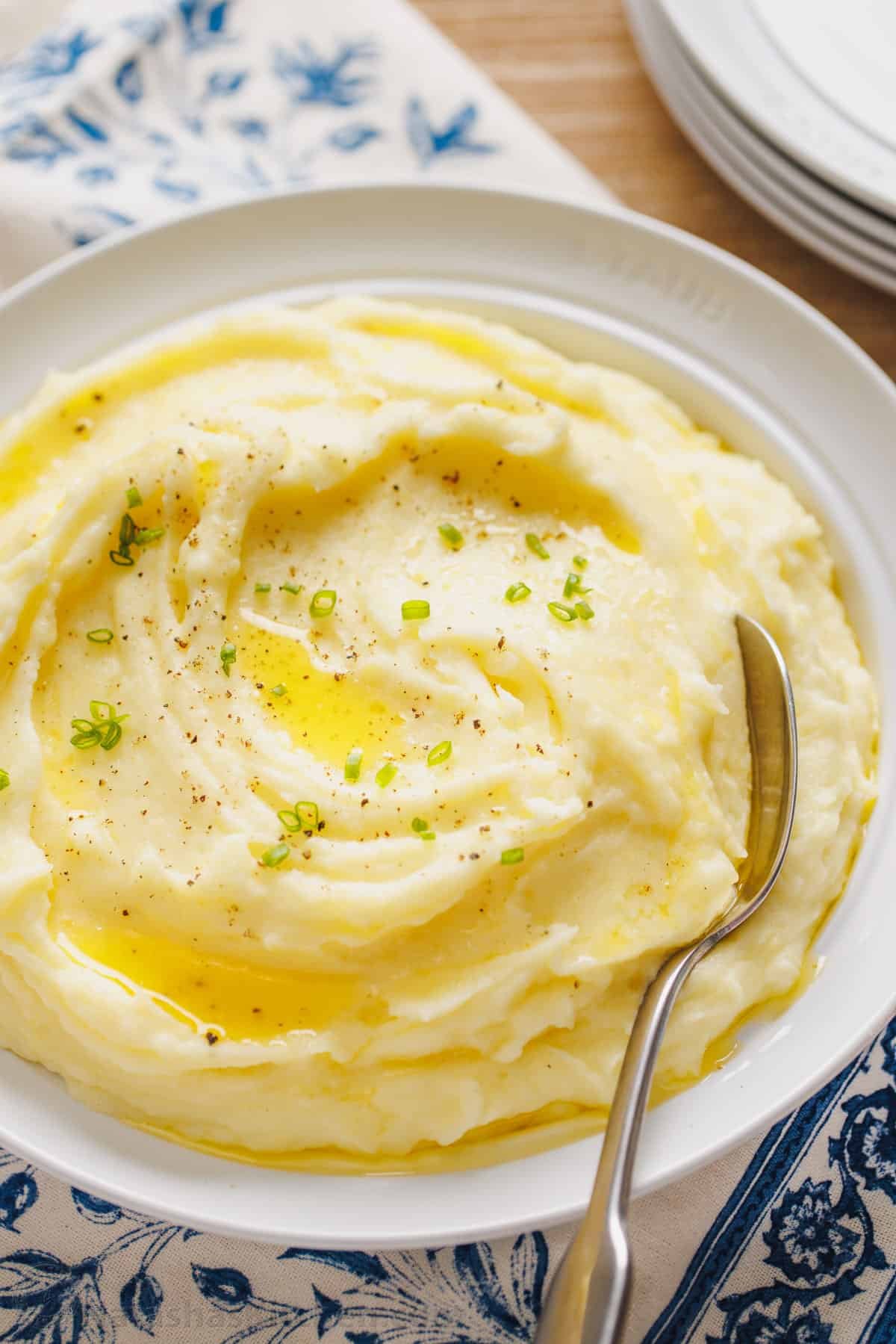 This is a simple sour cream mashed potatoes recipe with loads of buttery flavor. Enjoy homemade mashed potatoes as an easy, versatile side! A bowl of sour cream mashed potatoes topped with melted butter and freshly chopped chives, with a spoon.