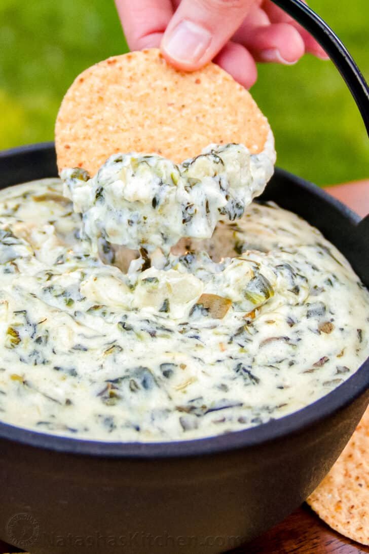Spinach Artichoke Dip is irresistibly creamy and loaded with spinach and artichokes. This is our go to dip for parties. It's an easy, excellent appetizer! #spinachartichokedip #spinachandartichokedip #spinachdip #artichokedip #dip #appetizer #natashaskitchen Spinach Artichoke Dip Recipe in Serving bowl with chip dipped inside