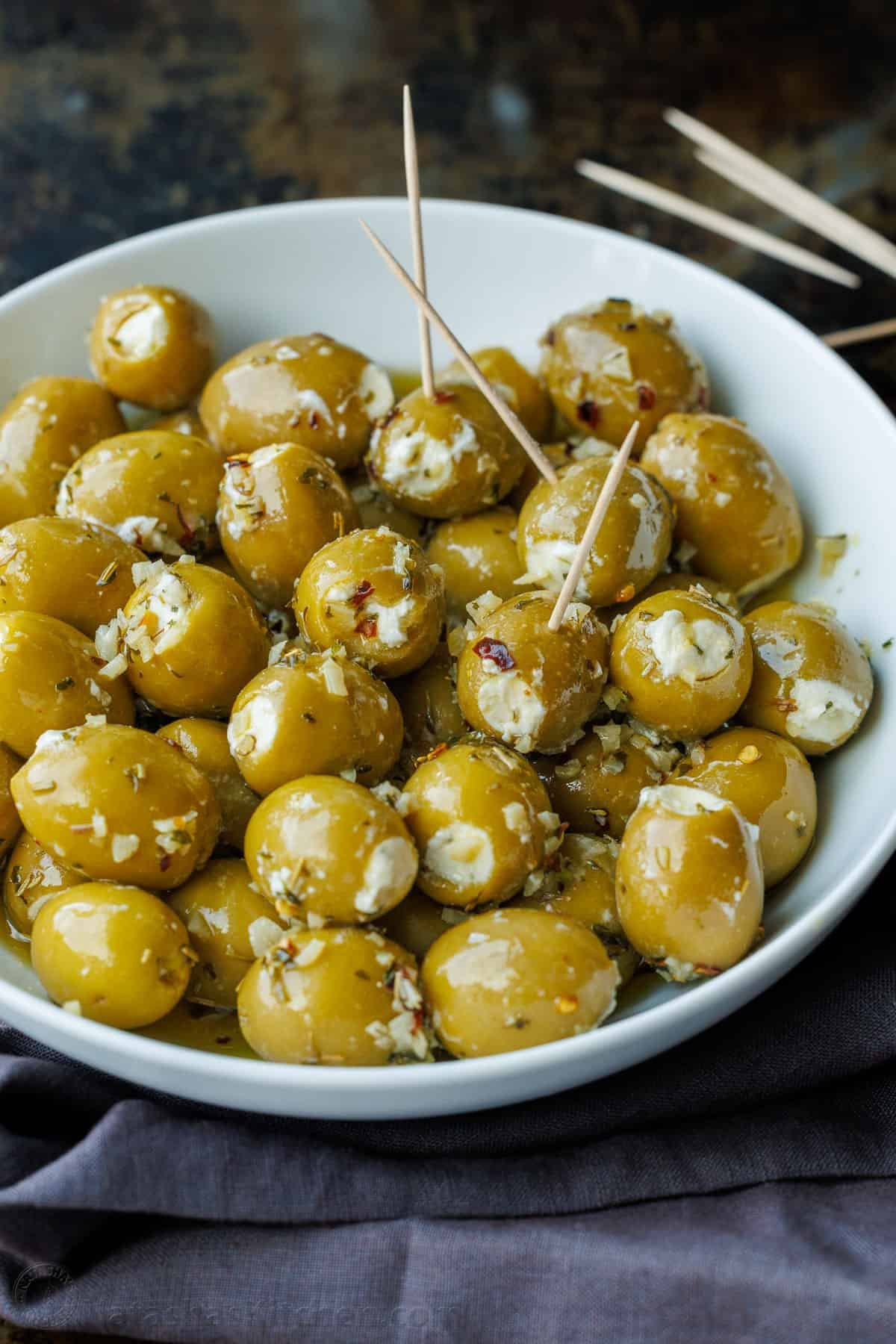 Stuffed Olives are the ultimate no-bake appetizer—quick to make, yet fancy enough for any occasion. They're filled with garlic and herb Boursin cheese and marinated in a flavorful garlic and herb olive oil. Stuffed green olives with white Boursin cheese, in a white bowl. Some olives have toothpicks for serving.