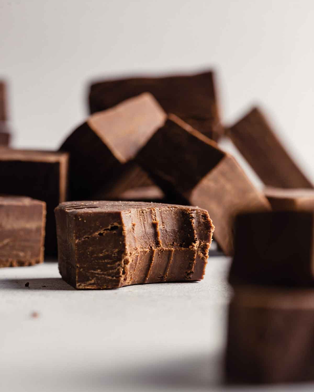A single piece of chocolate fudge with a bite taken out, with other squares of fudge in the background.