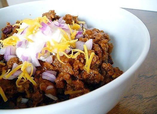 Chili topped with sour cream, onions, and shredded cheese in a white bowl.