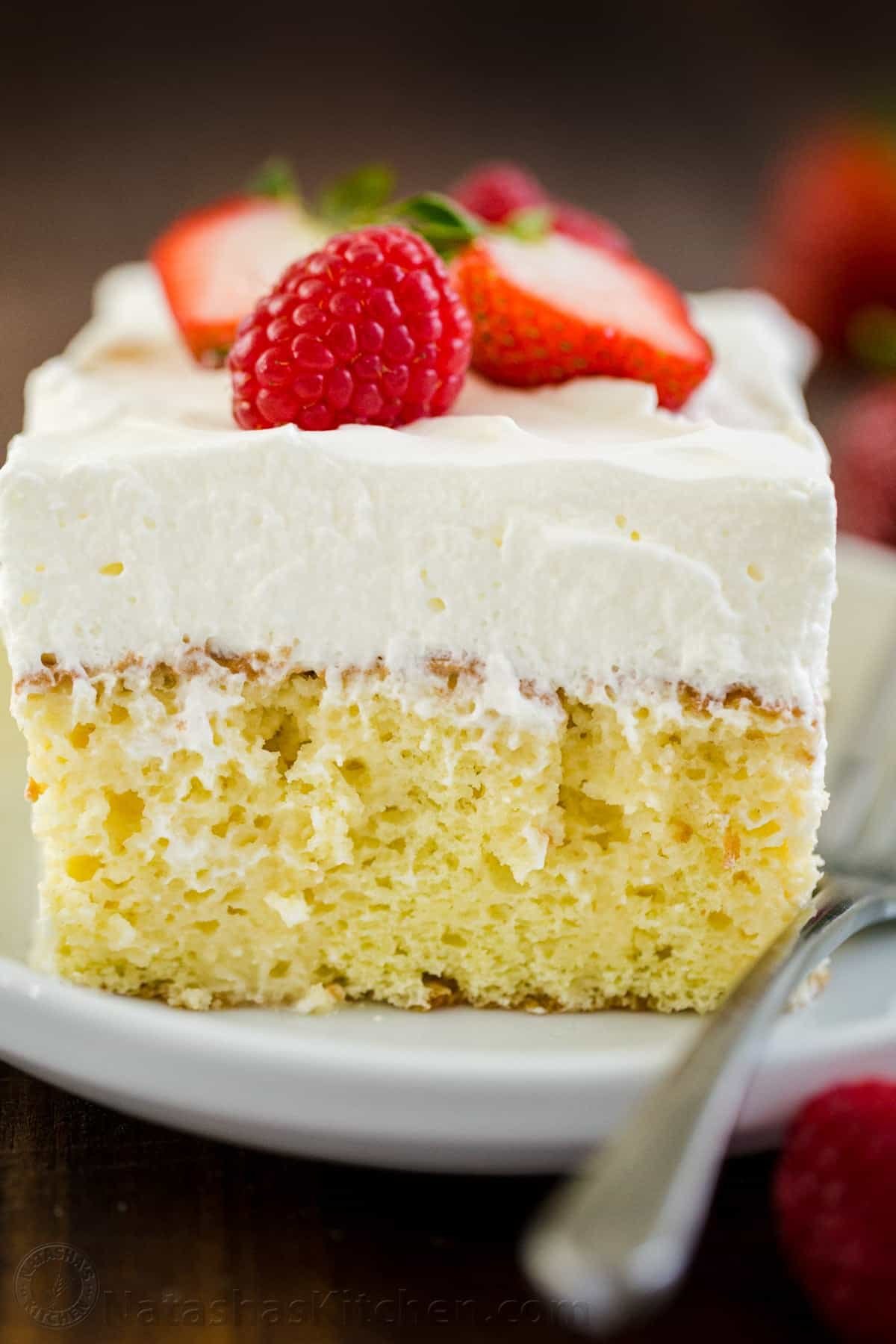 Tres Leches Cake has a soft and ultra-moist crumb. This authentic Tres Leches Cake recipe is soaked with a 3 milk mixture and topped with whipped cream. #tresleches #treslechescake #treslechescakerecipe #mexicancake #cake #cakerecipe #moistcake #natashaskitchen Slice of Tres Leches Cake on a plate with fork