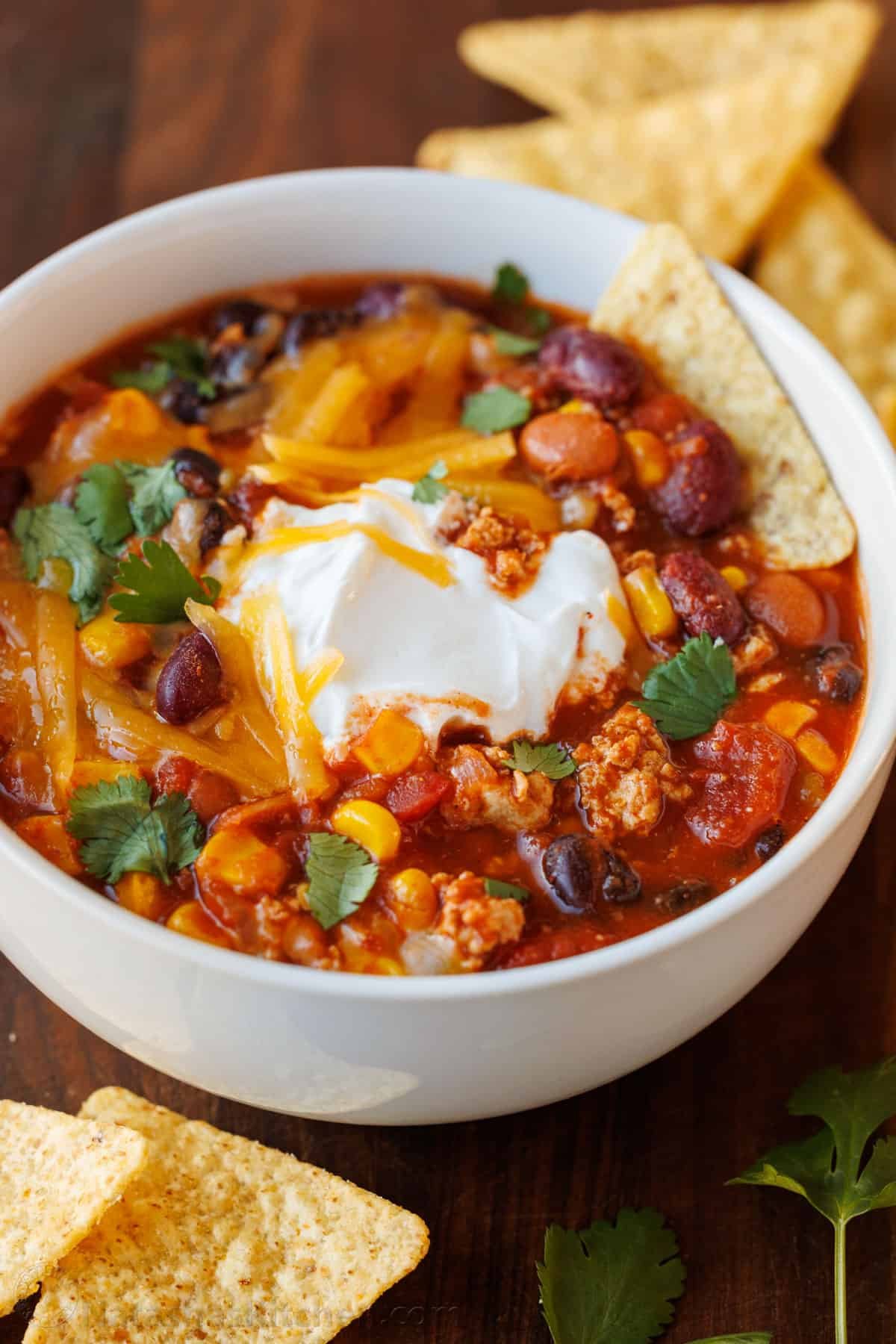 The best Turkey Chili recipe - easy (mostly dump & simmer) and loaded with turkey, beans, and veggies. It's perfect for busy weeknights! Bowl of the best turkey chili recipe with tortilla chips on the side