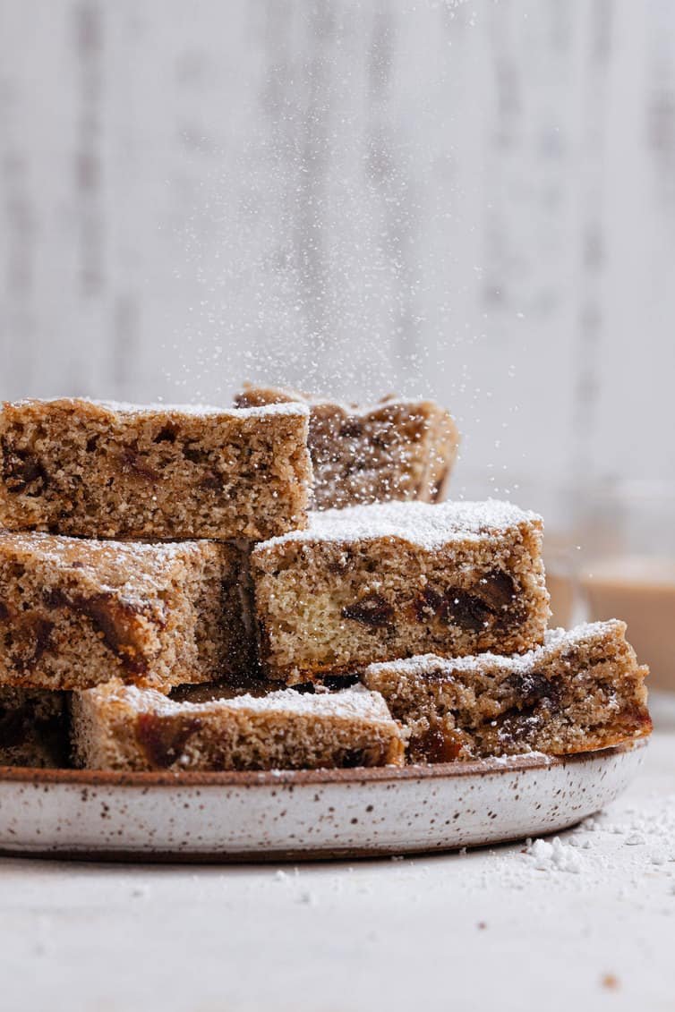 Date bars stacked on a plate and sprinkled with powdered sugar.