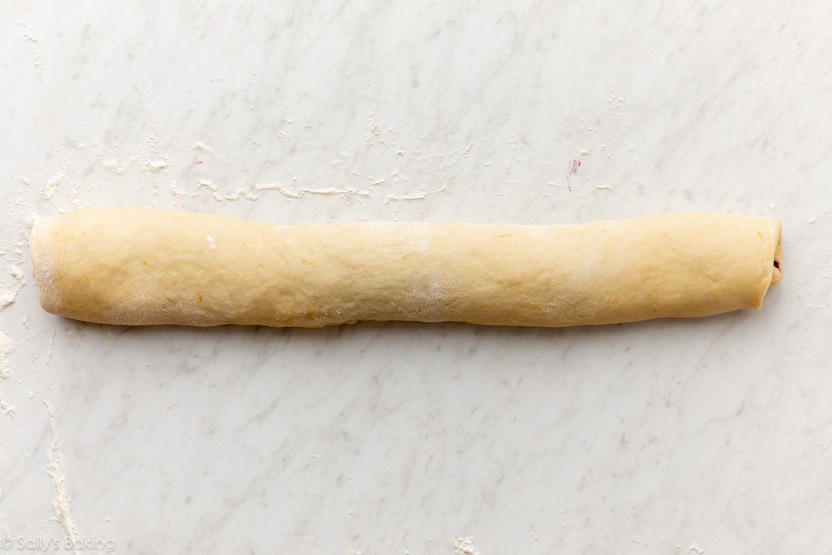 dough rolled up into a log on a marble surface.