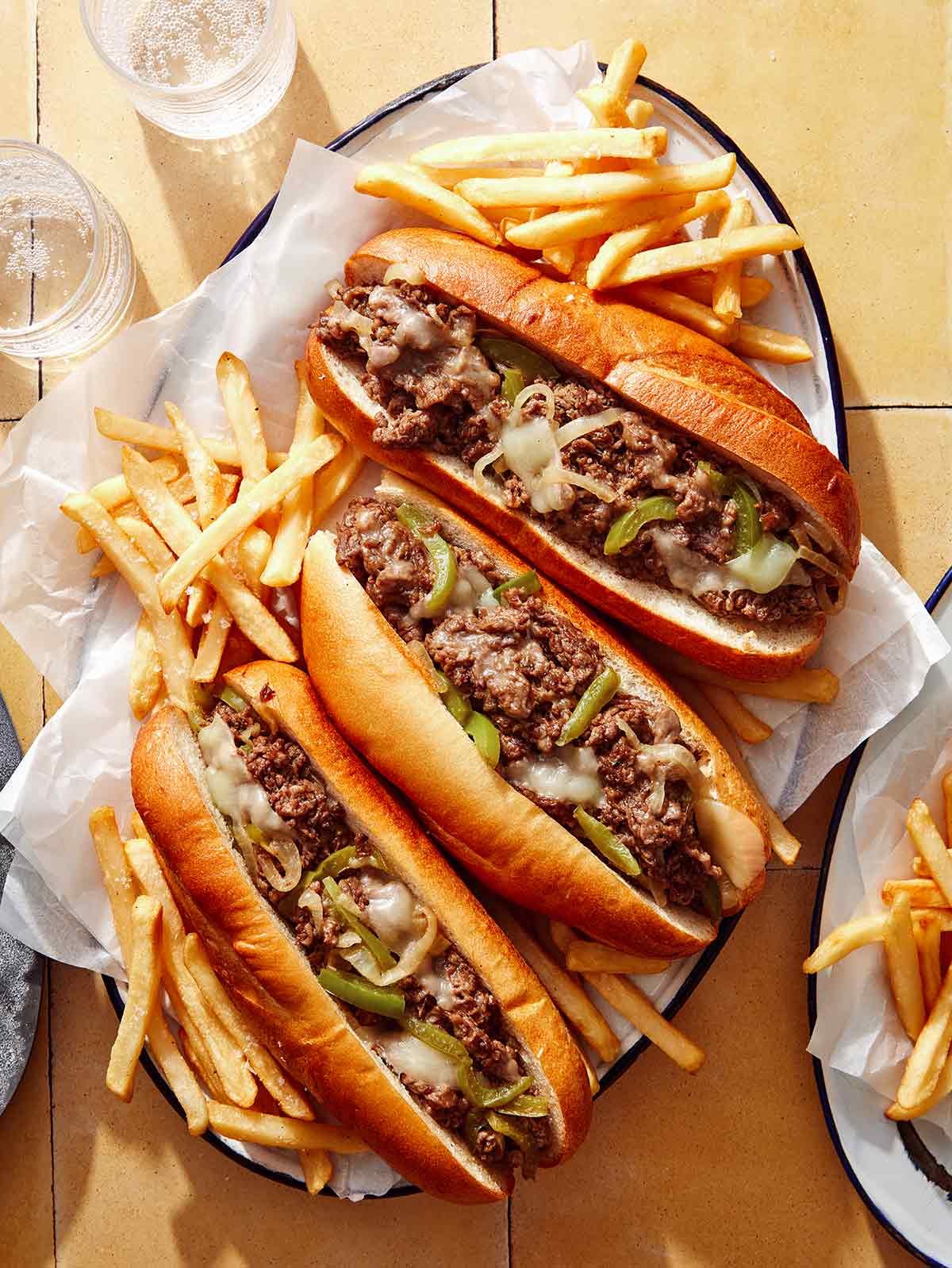 Philly cheesesteak sandwiches with french fries next to them and water.