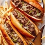 Philly cheesesteak sandwiches with french fries next to them and water.