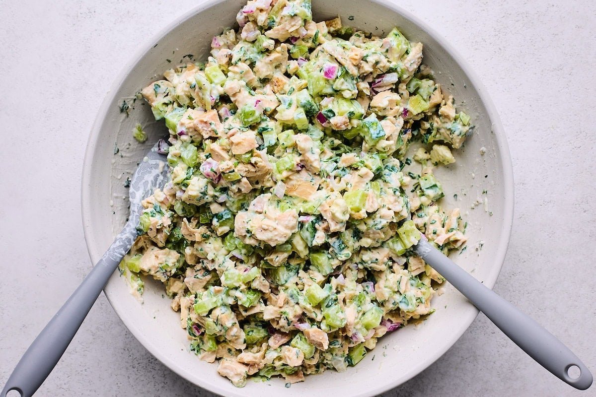 tzatziki chicken salad being stirred together in bowl with two spatulas.
