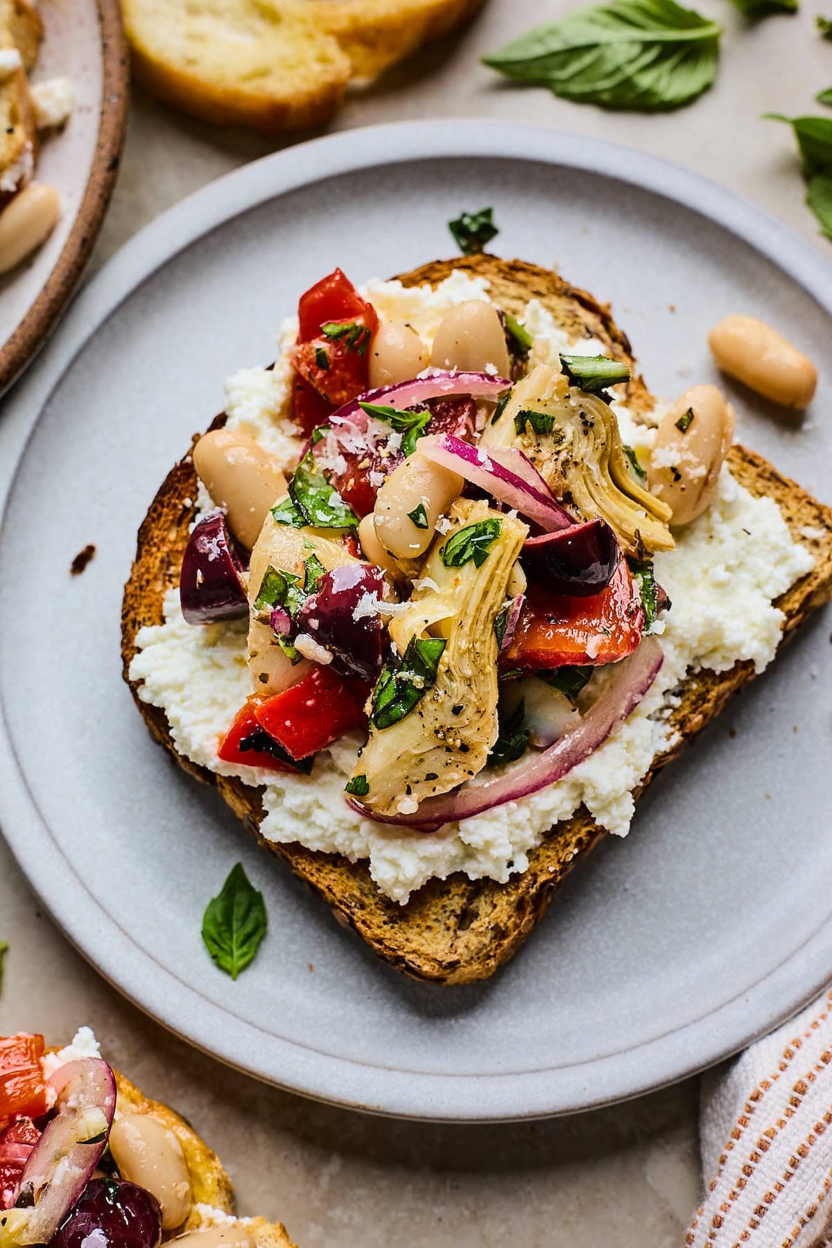 marinated artichoke, roasted red pepper, and white bean salad on ricotta toast with fresh basil.