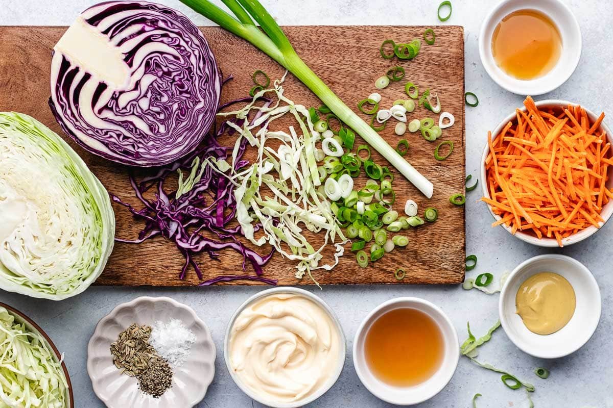 cabbage and green onion on cutting board and ingredients in bowls to make coleslaw.