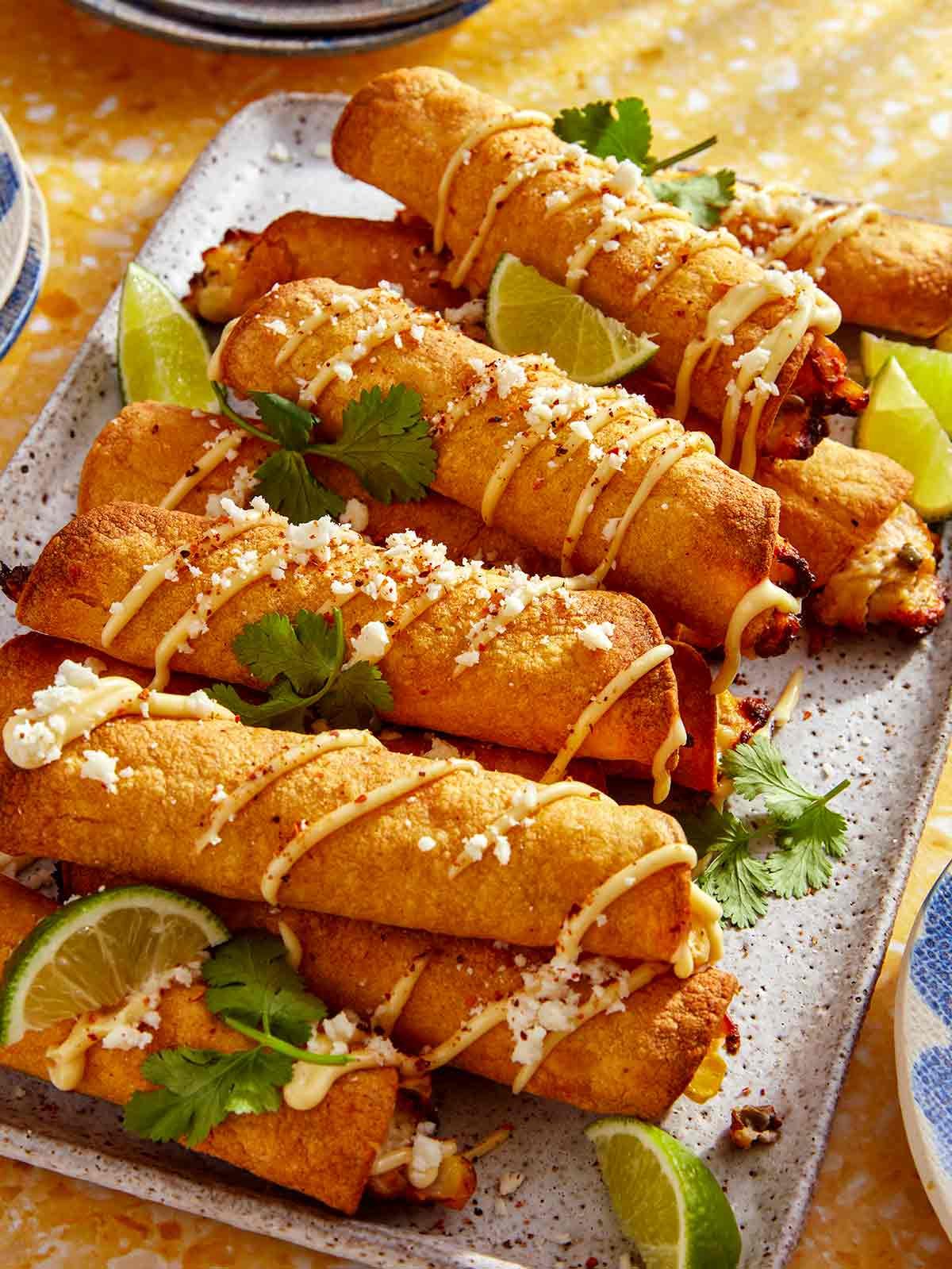 Taquitos stacked on a platter with toppings.