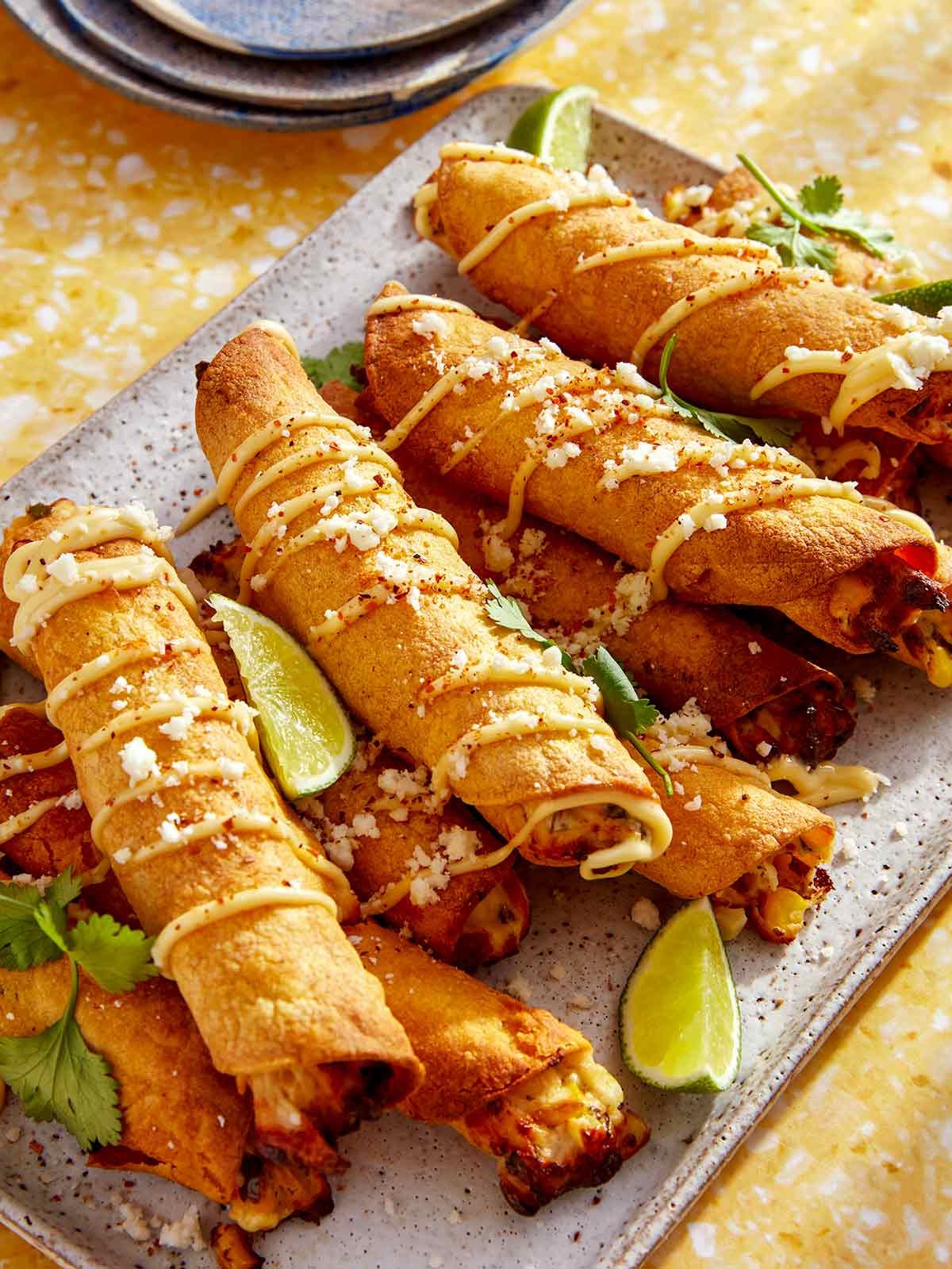 Taquitos on a platter with plates in the background.